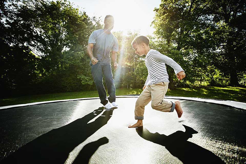Smiling father and young son jumping on trampoline.